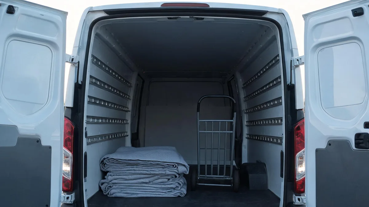 Pusta ładownia busa z otwartymi drzwiami, w środku złożone koce i metalowy wózek transportowy